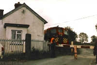 Another view of Carrolls Cross, showing the level crossing and the rear of the station building with loco No.159 passing in June 1985. The station has since been rebuilt and crossing gates removed. ©David Parks