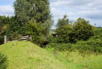 Viewed from the old railway embankent on the approach to the former River Dinin bridge south of Dysart crossing. This view is looking north towards Castlecomer. The bridge abutments have been partially blocked by railway sleepers recovered from the track lifting nearly fifty years ago.