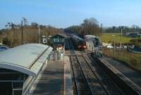An older generation of diesel railcar, represented by an orange liveried &#39;Arrow&#39; 2800 Class approaches the station with a service to Maynooth. On the left can be seen the newer modern booking office, a common feature on the Maynooth line.