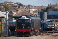 A Class loco No.A39 is seen preparing to back onto a train at Downpatrick Station. The loco is seen standing beside the boundary gate of the railway with Downpatrick town in the background.