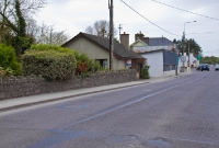 A view looking across the road towards Baltmore at the former Drimoleague level crossing. A bungalow has been built on the former trackbed. The corrugated iron structure in the background was once a garage, which was in use during railway days.