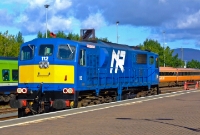 The blue livery of Northern Ireland Railway&#39;s 111 Class loco No.112 gleams in the sun as it runs around a Railway Preservation Society of Ireland special at Dundalk Station. Behind in the sidings is a 29000 Class railcar, and a rake of Mk3 carriages.