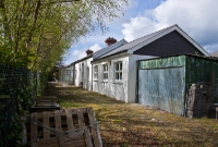 This is the eastern end of Dunmanway Station, looking west towards Cork. The building, now a veterinary clinic, has been extended at this end of the station. A fence and a line of trees mark the egde of the disused platform.
