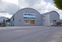 This is the site of the level crossing at the west end of Dunmanway Station, where the railway line crossed the R599 road leading into the town. The large corrugated iron building seen here has been built across the former trackbed to Bantry.