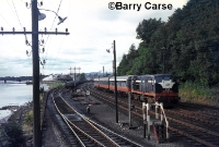 Viewed from Waterford West signal cabin in the early 1970s, a 141 Class loco No.B158, approaches Waterford yard with an AEC railcar in tow from Limerick. The bracket signal visble to the left of the train read for the lines to Mallow, Limerick and Dublin respectively. ©Barry Carse