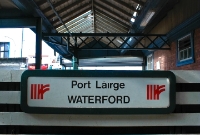 Waterford Station name board, complete with 1990s style Irish Rail &#39;point&#39; logos. Behind can be seen part of the 1906 GSWR constructed brick station building and canopies.