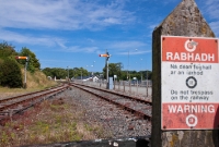 Wellingtonbridge, looking east towards Rosslare, showing the &#39;down&#39; starting semaphore signals, as well as an old CIE mispelled &#39;iarnród&#39; warning sign. A gated level crossing is located at this end of the station.