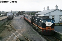 Seen at the same location but over 30 years earlier, 141 Class loco No.B155, in CIE&#39;s black &#38; tan livery, stands at Wellingtonbridge with a Rosslare Harbour bound service. Visible on the left is the sugar beet loading bank and small goods shed. ©Barry Carse